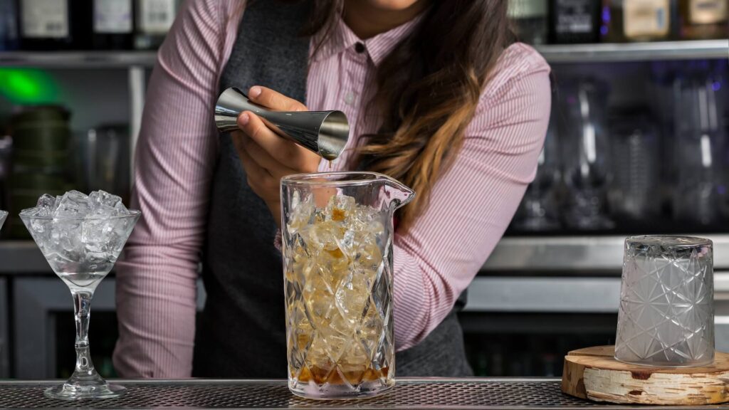 Bartender preparing a cocktail using a crystal mixing glass filled with ice and a jigger for measuring