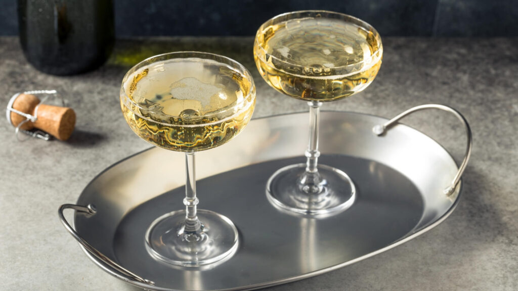 Two coupe glasses filled with champagne on a silver tray with cork