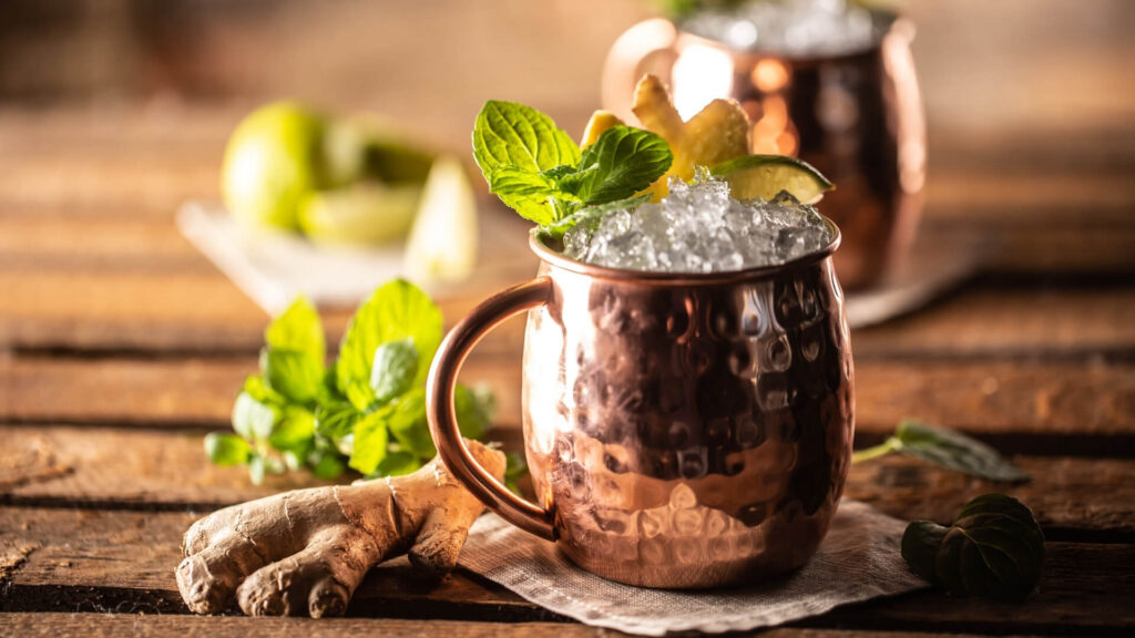Moscow Mule cocktail served in a copper mug with mint, lime, and crushed ice on a rustic wooden table.